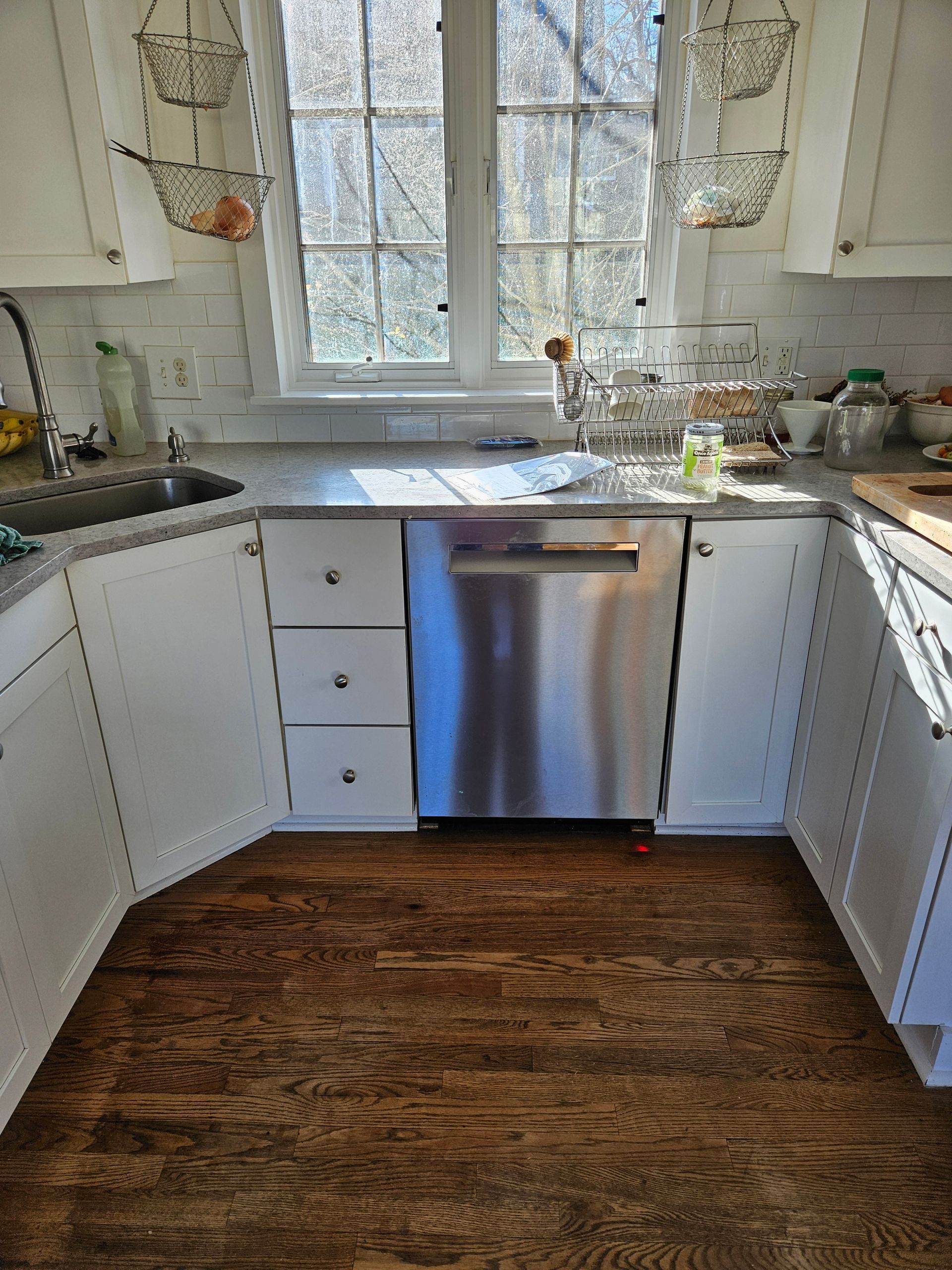 Open dishwasher with two racks. White cabinets, black countertop, built-in oven.