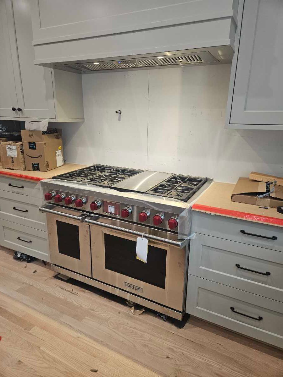 Man in blue overalls installing a black stovetop in a kitchen.