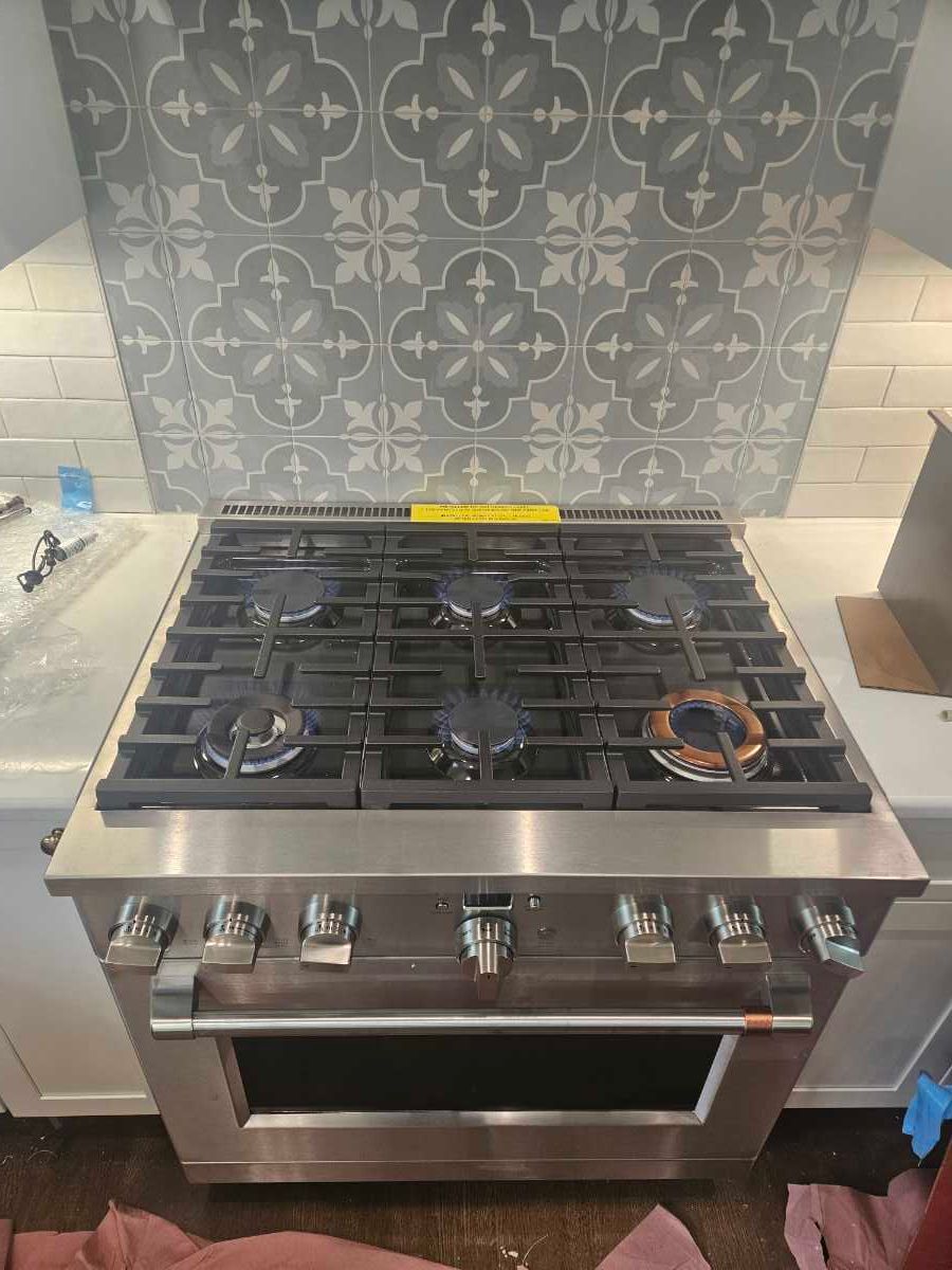 Two movers in blue overalls using a hand truck to move a large, wrapped object in a white kitchen.