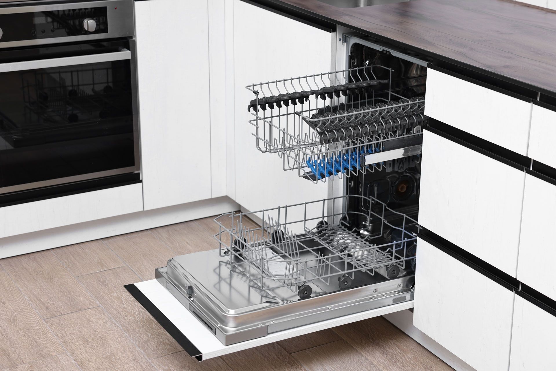 Open dishwasher with two racks. White cabinets, black countertop, built-in oven.