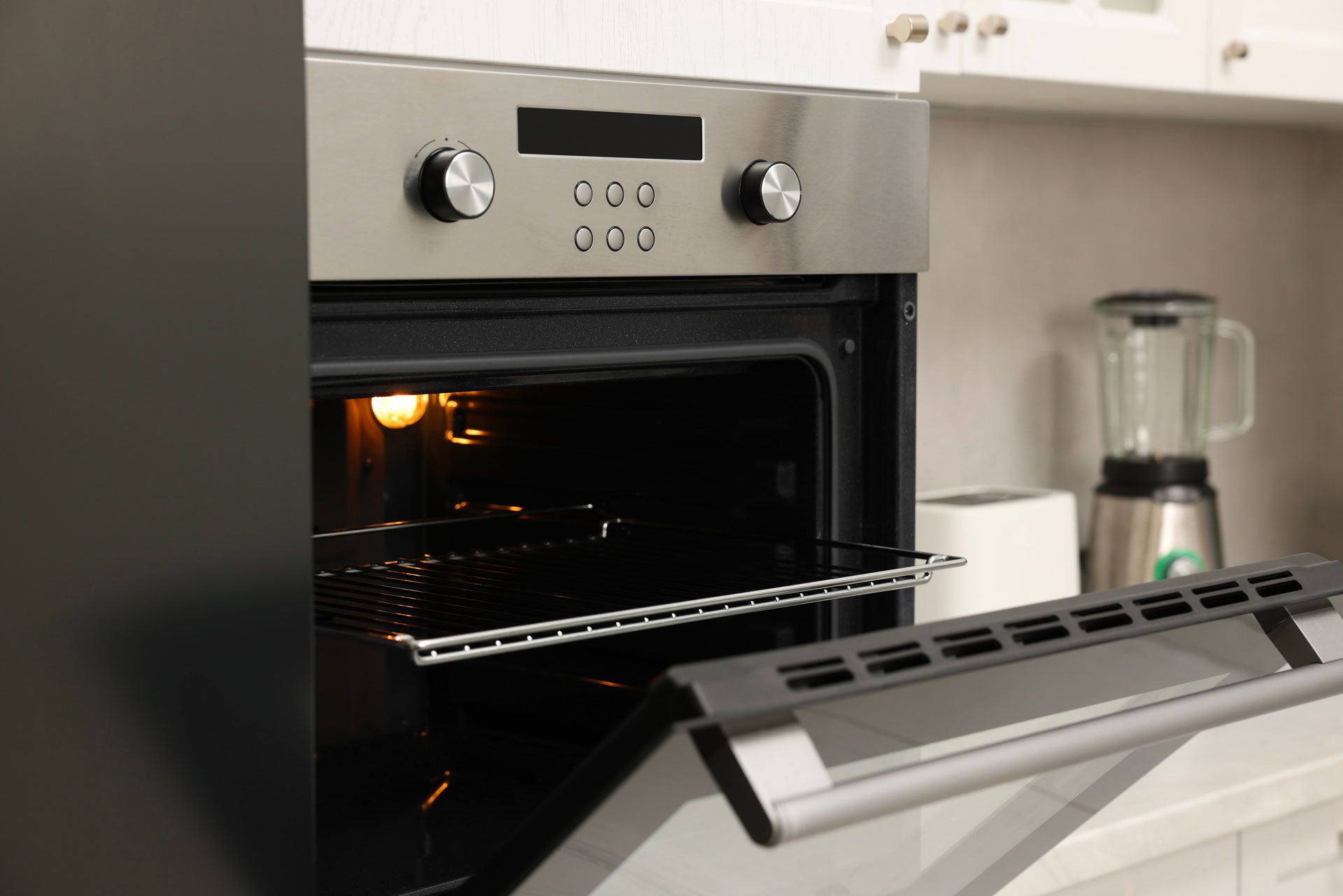 Open oven with a rack inside, in a white kitchen setting.