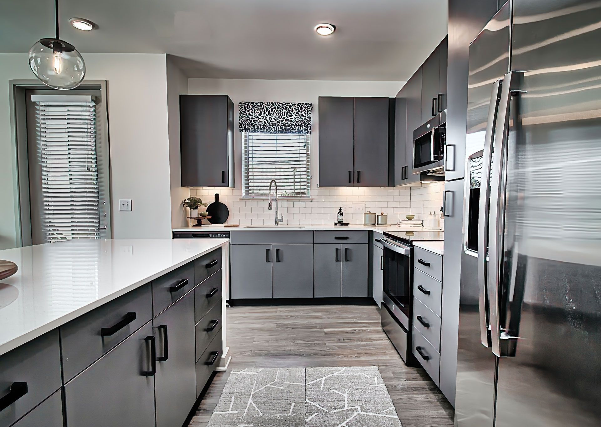 Modern gray kitchen with stainless steel appliances, white countertops, and patterned rug.