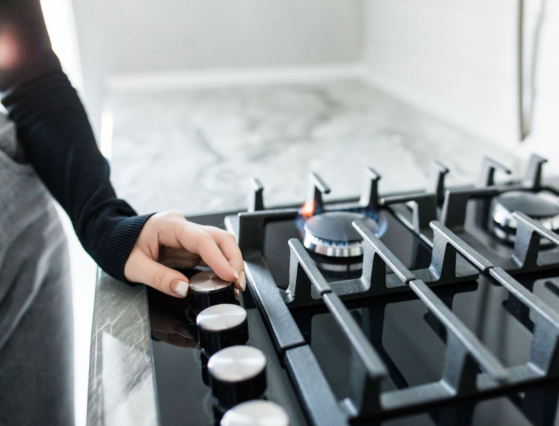 Hand turning a knob on a gas stovetop, with one burner lit, on a countertop.