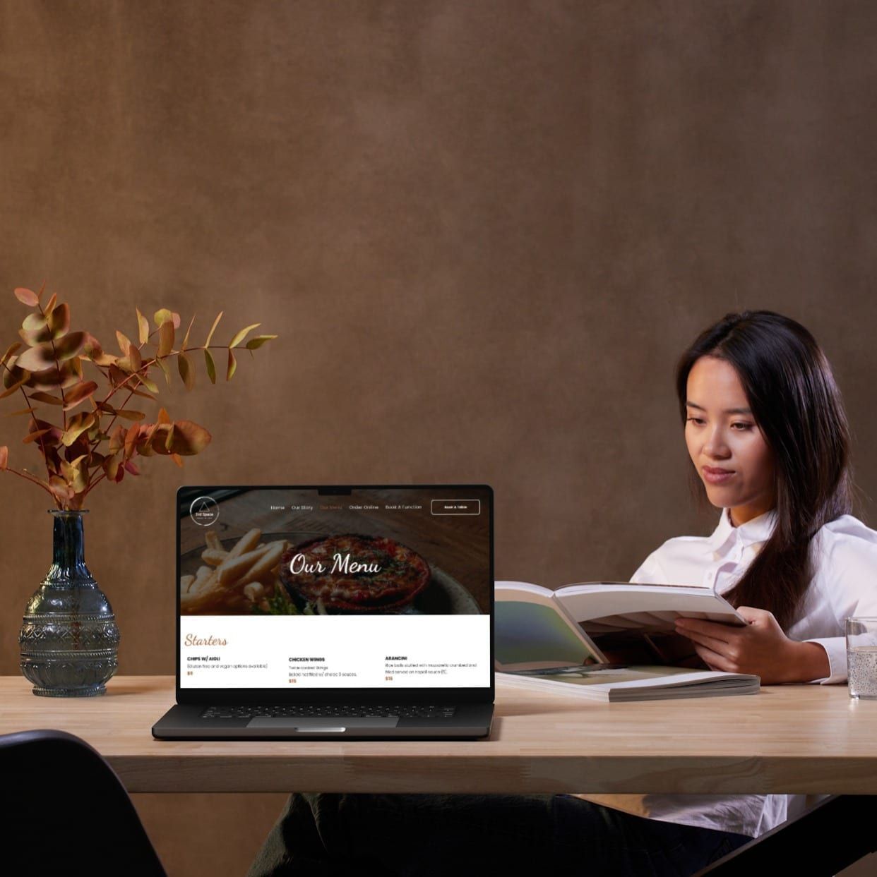 A woman is sitting at a table with a laptop and a book.