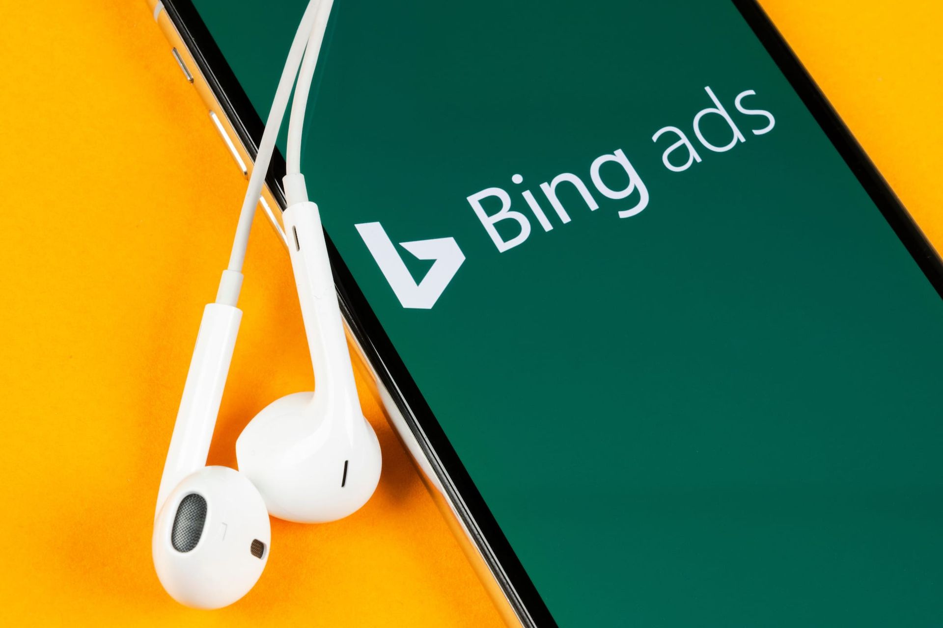 A cell phone with headphones attached to it and the bing ads logo on the screen.