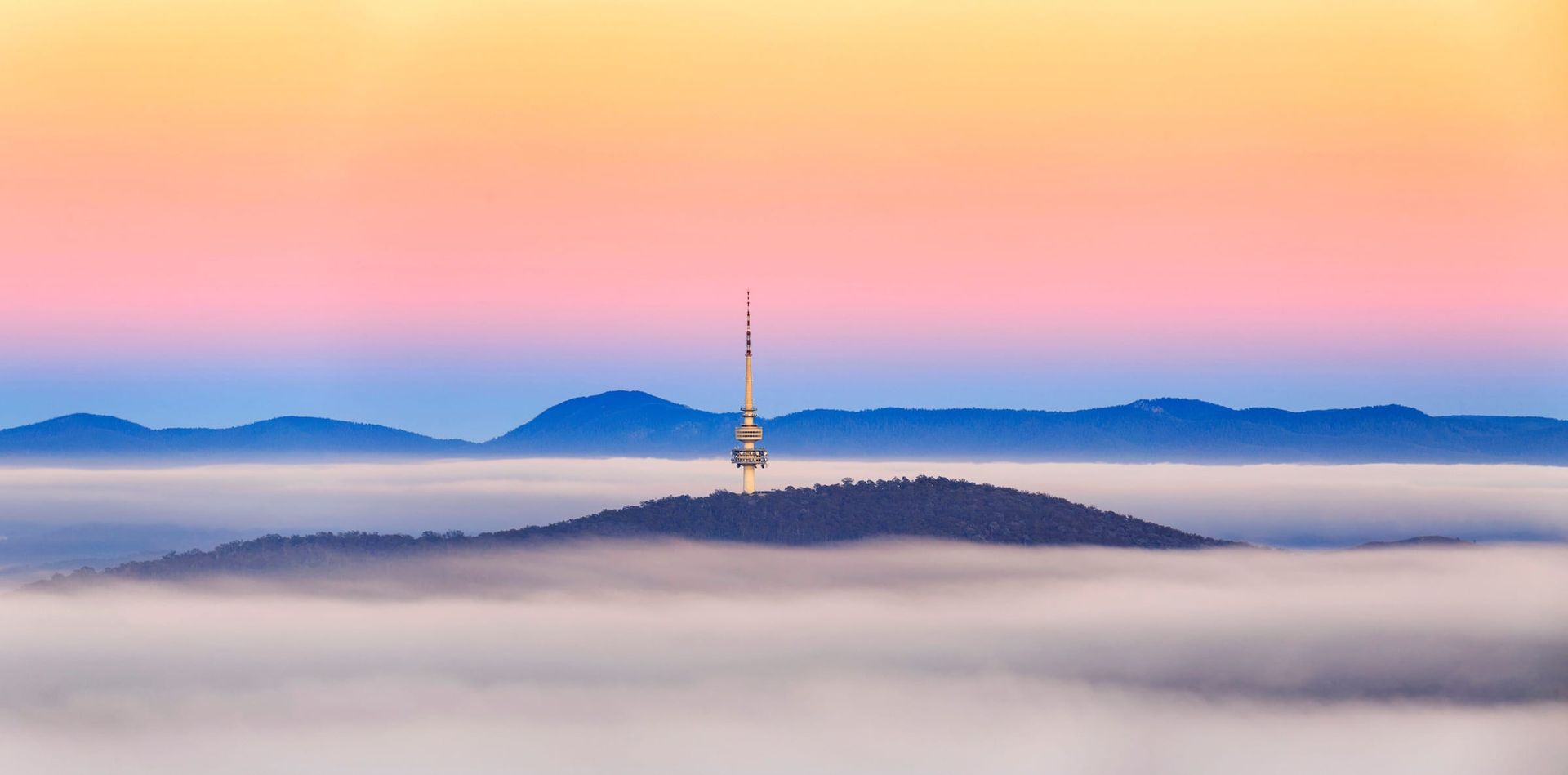A tower in the middle of a foggy valley with mountains in the background.
