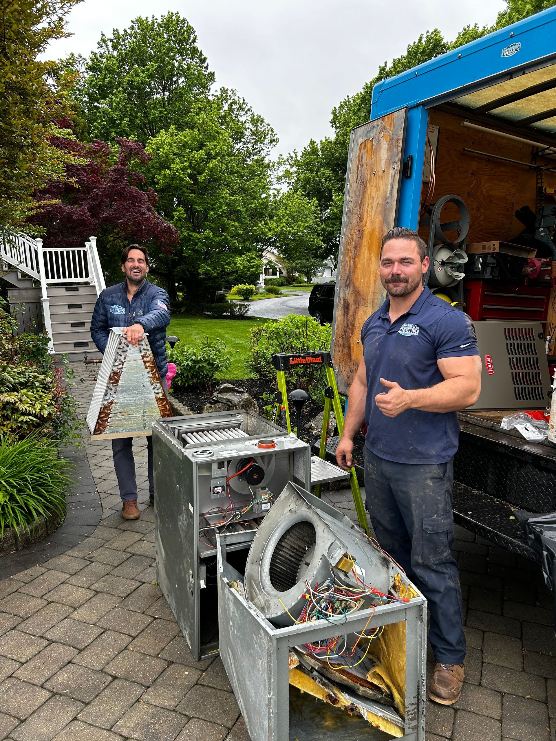 Two people beside an open trailer, unloading metal frames in a backyard garden.