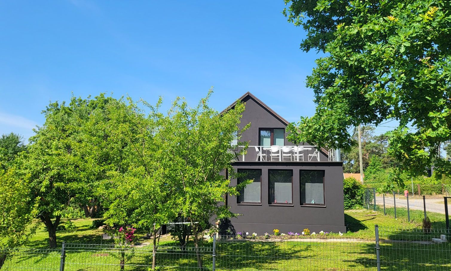 A house with a balcony on top of it is surrounded by trees and grass.