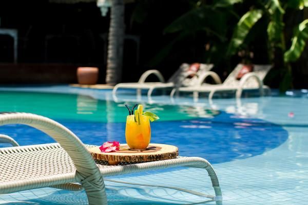 Uma espreguiçadeira de vime está ao lado de uma piscina com uma bebida em uma bandeja.