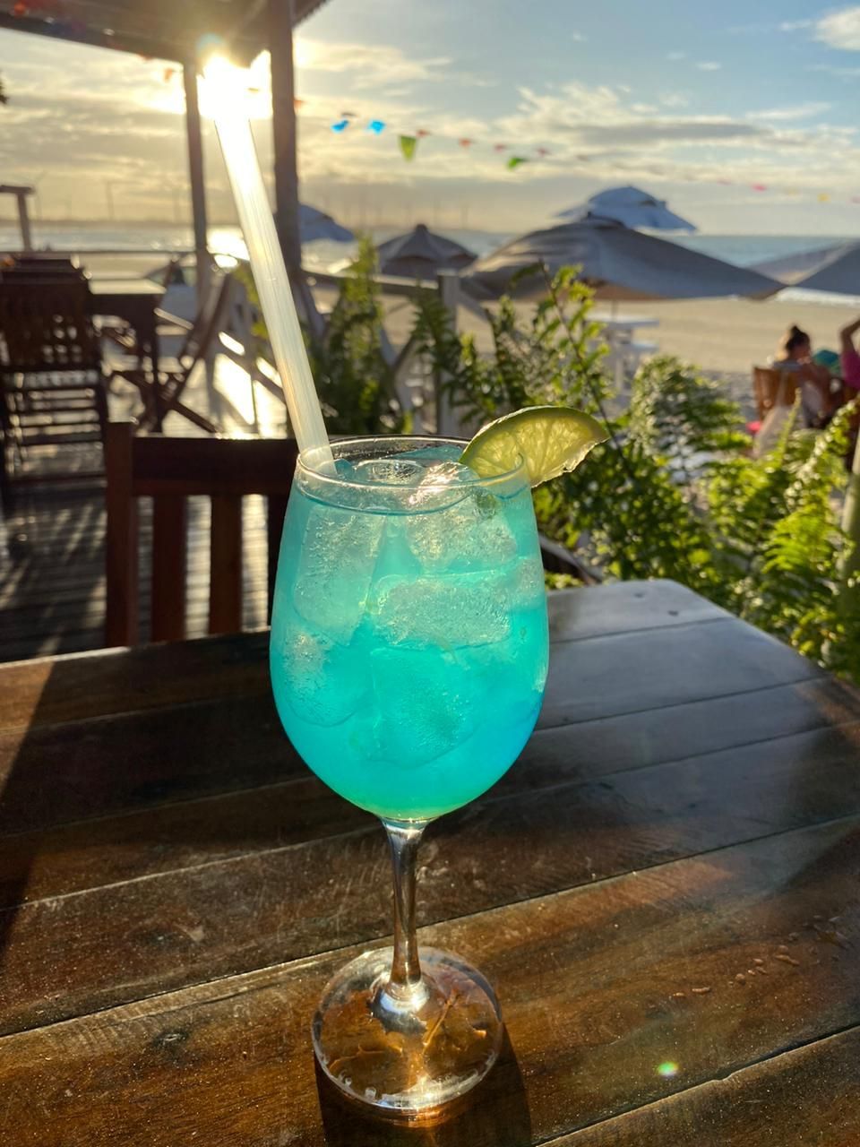 Uma bebida azul em uma taça de vinho com canudo sobre uma mesa de madeira.