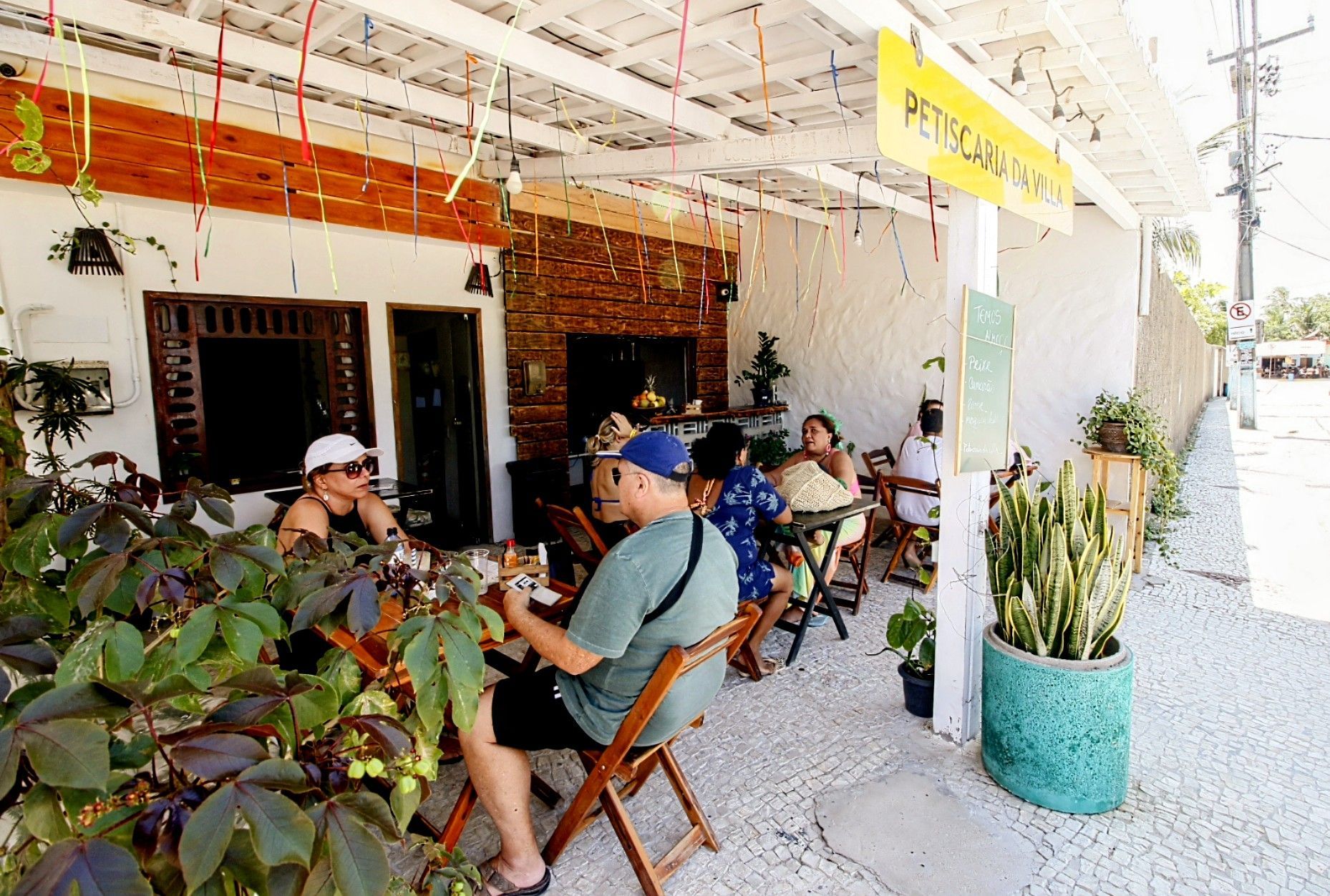 Um grupo de pessoas está sentado em mesas do lado de fora de um restaurante.