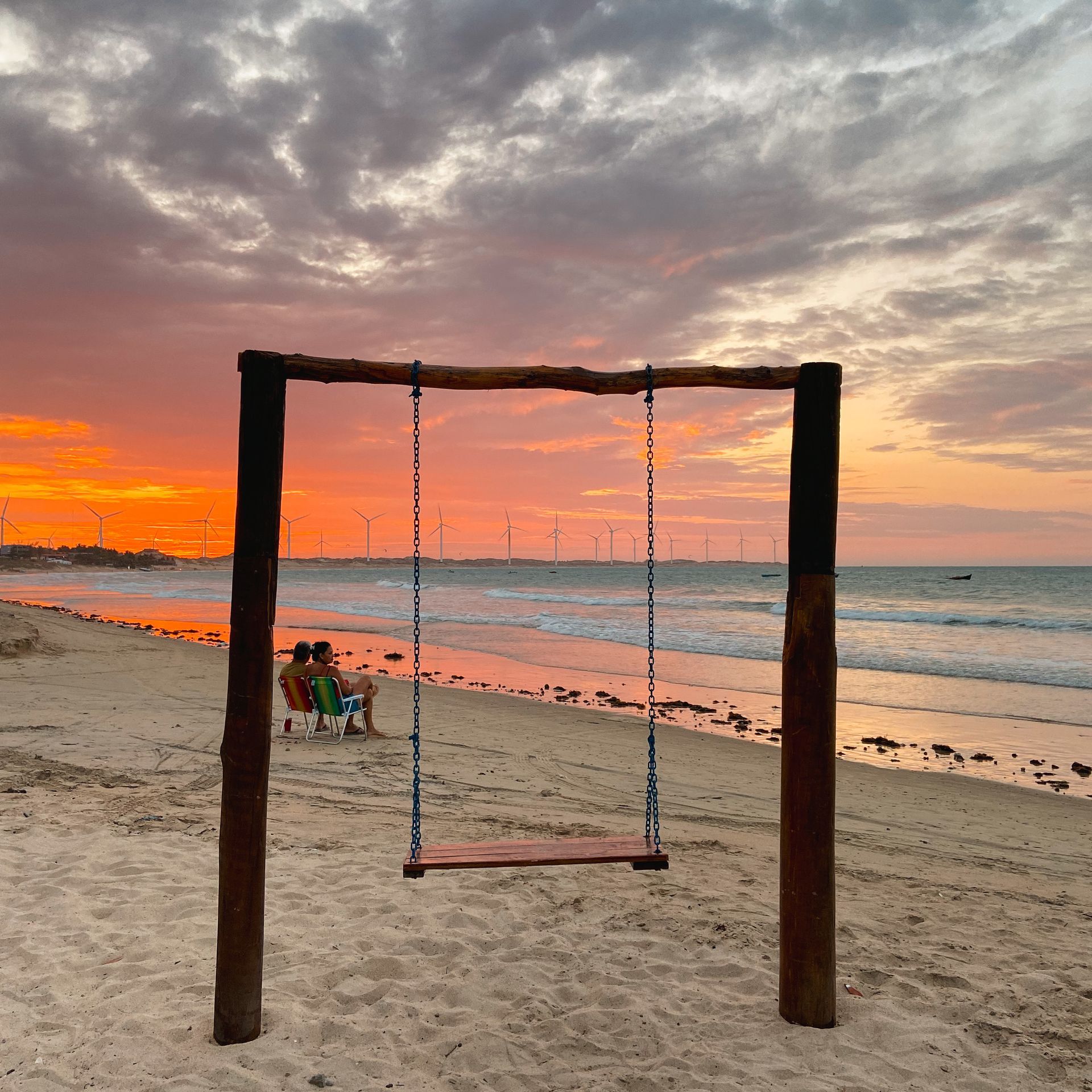 Um balanço de madeira em uma praia com um pôr do sol ao fundo