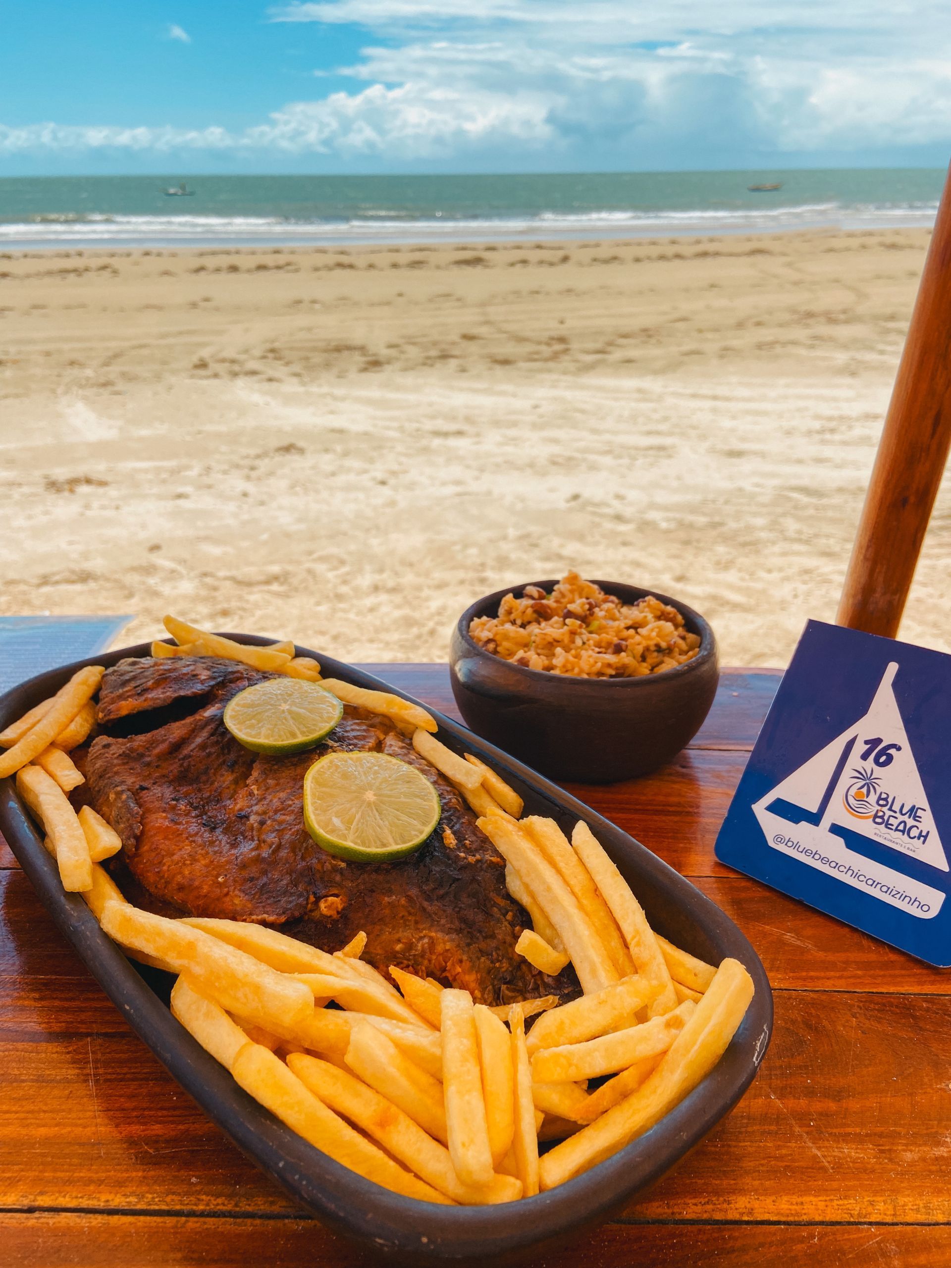 Um prato de comida com batatas fritas e uma tigela de arroz em uma mesa em frente à praia.