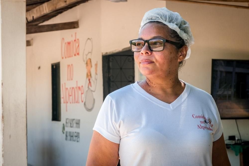 Uma mulher de óculos e chapéu branco está parada em frente a um prédio.