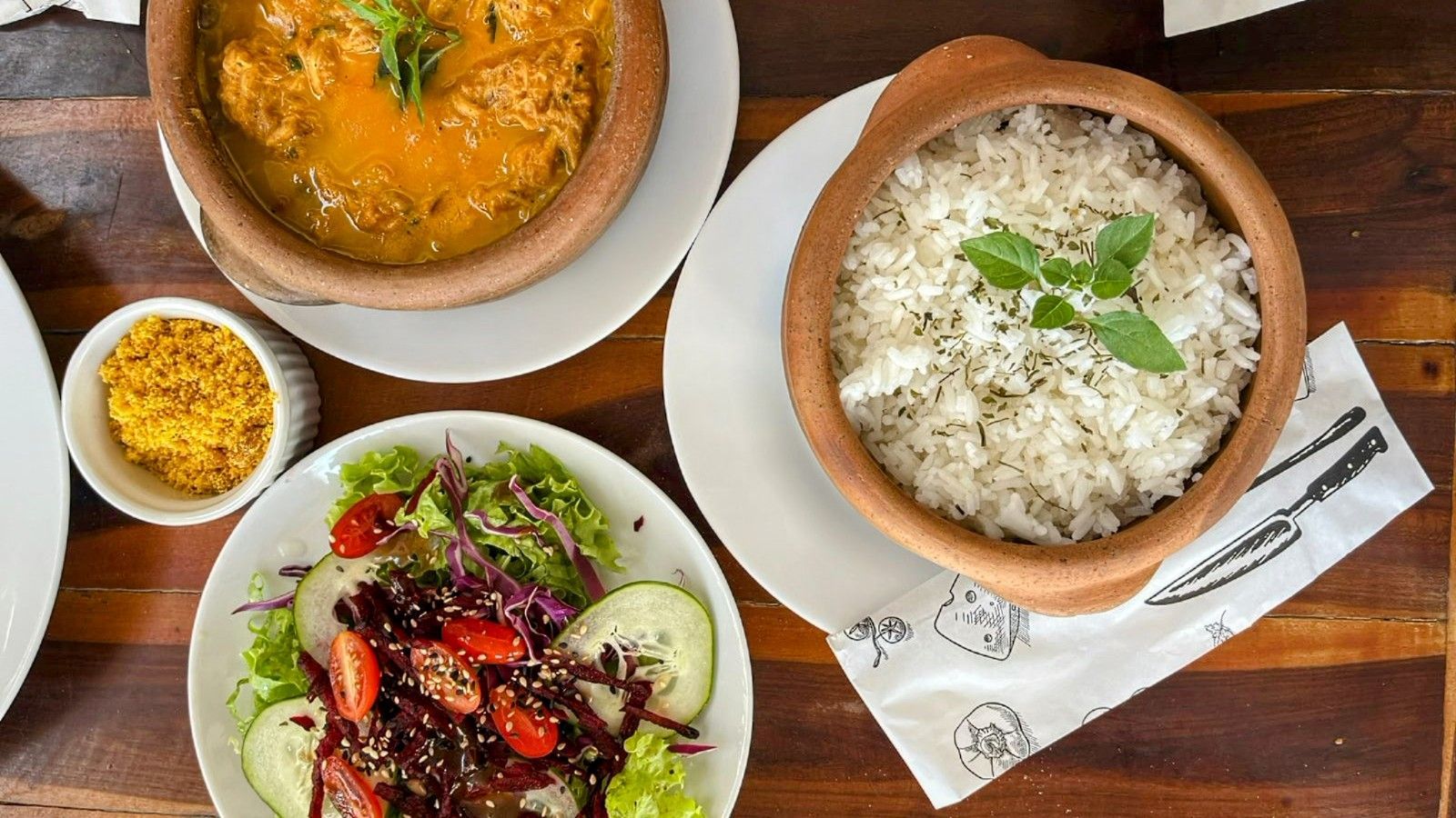 Uma mesa de madeira com pratos de comida e tigelas de arroz.