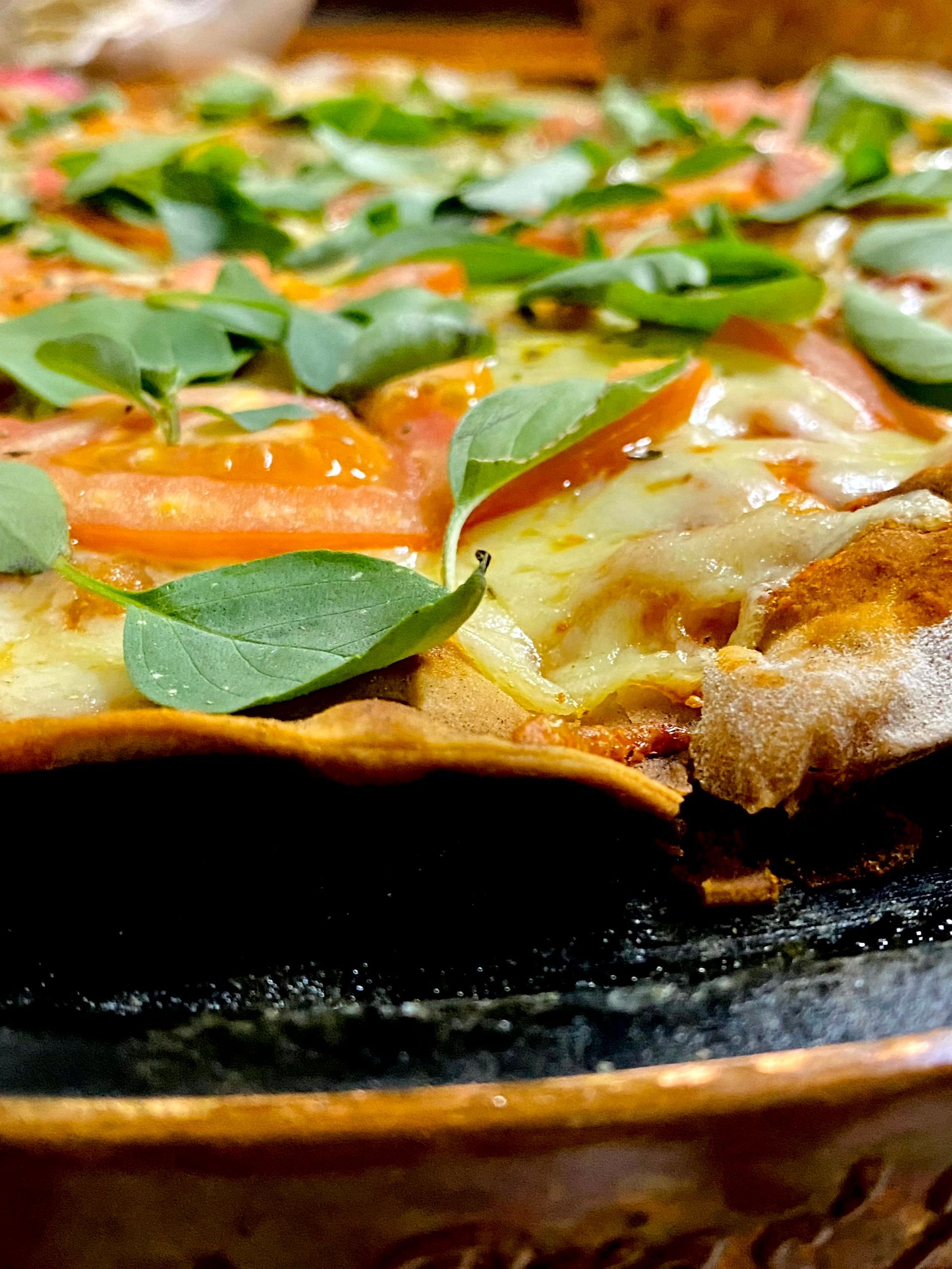 Um close de uma pizza com tomate e manjericão em uma panela.