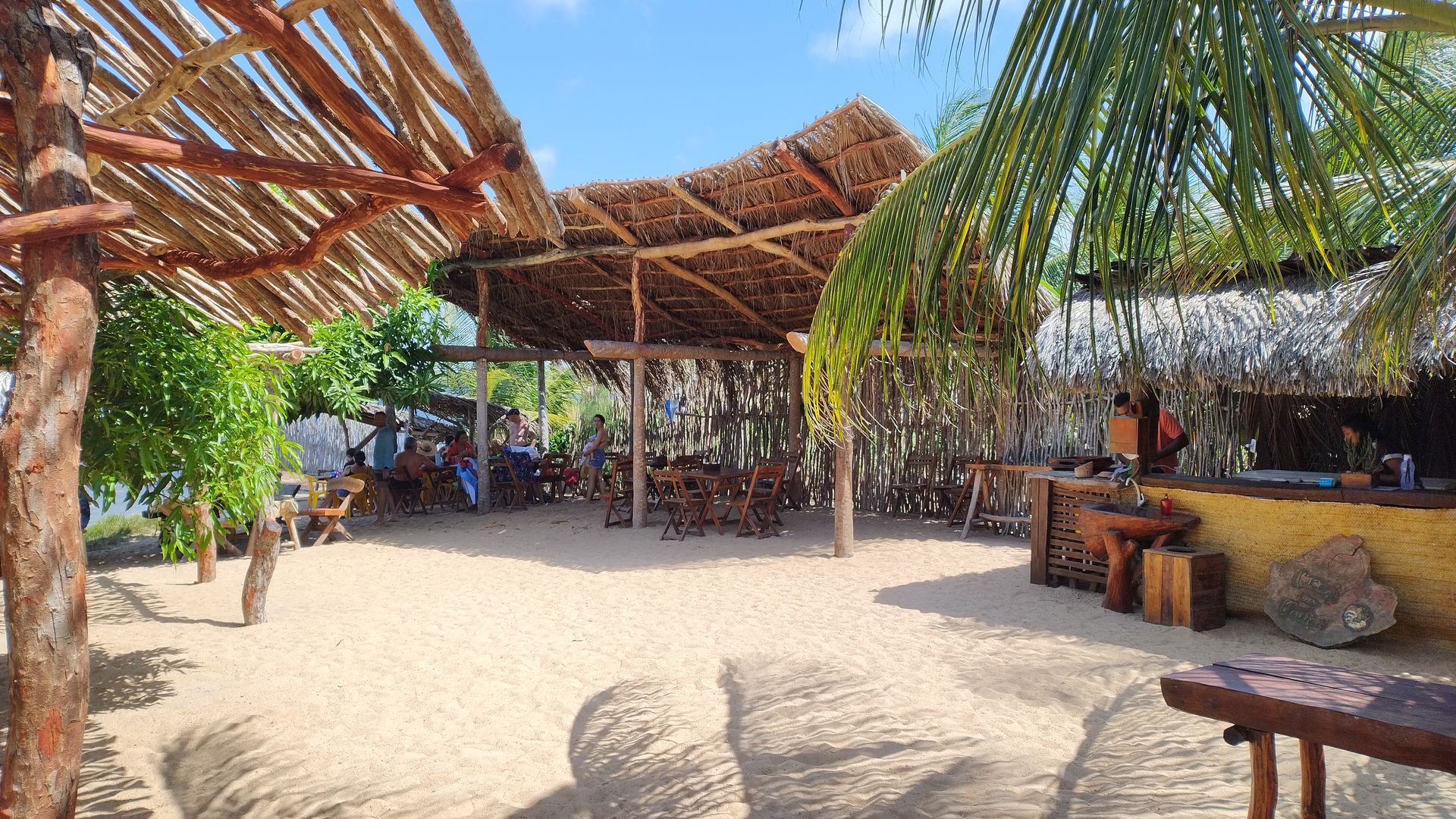 Um restaurante na praia com mesas e cadeiras sob telhado de palha.