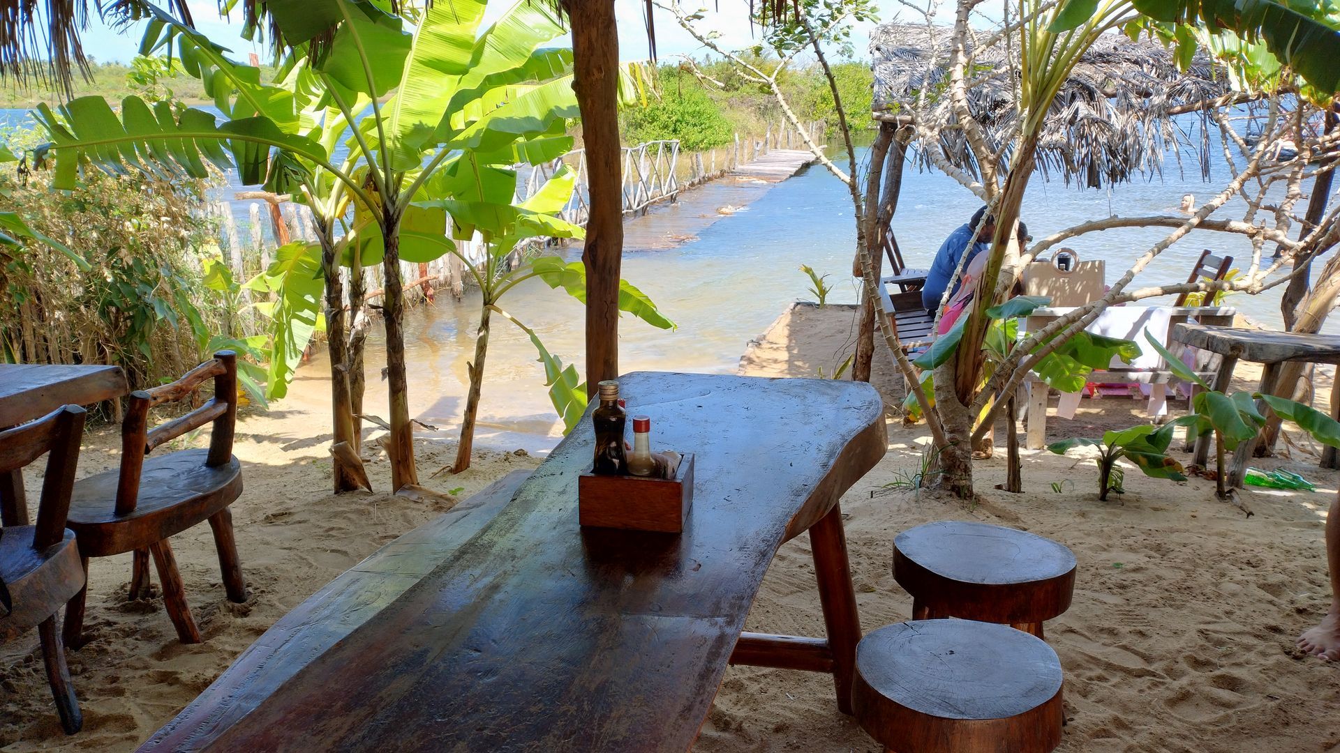 Uma mesa e cadeiras de madeira em uma praia perto de um rio