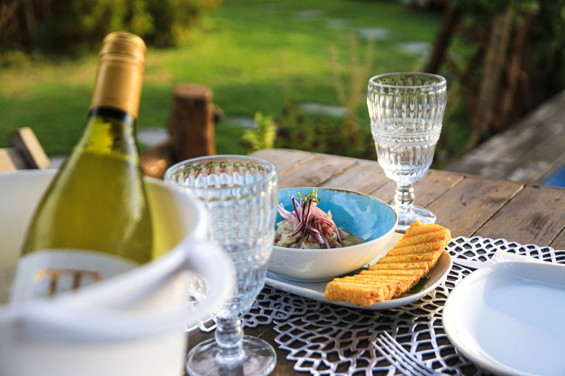 Uma garrafa de vinho está sobre uma mesa de madeira ao lado de um prato de comida.