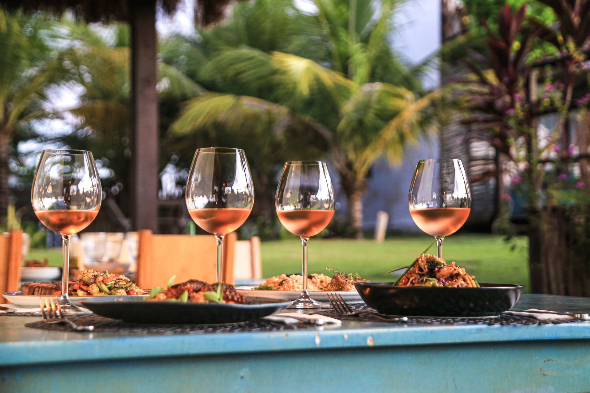 Quatro taças de vinho estão sobre uma mesa com pratos de comida.