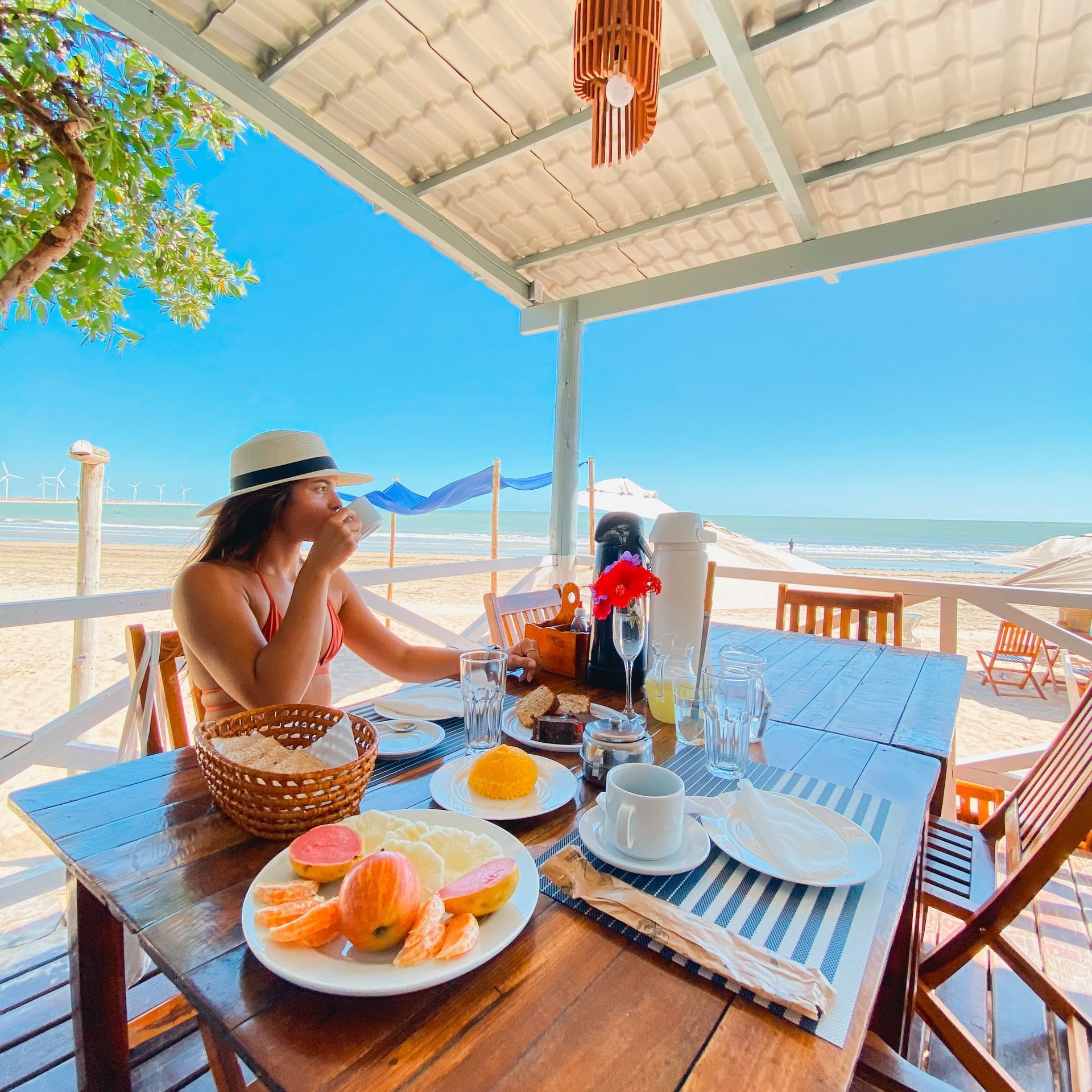 Uma mulher está sentada em uma mesa comendo comida na praia.