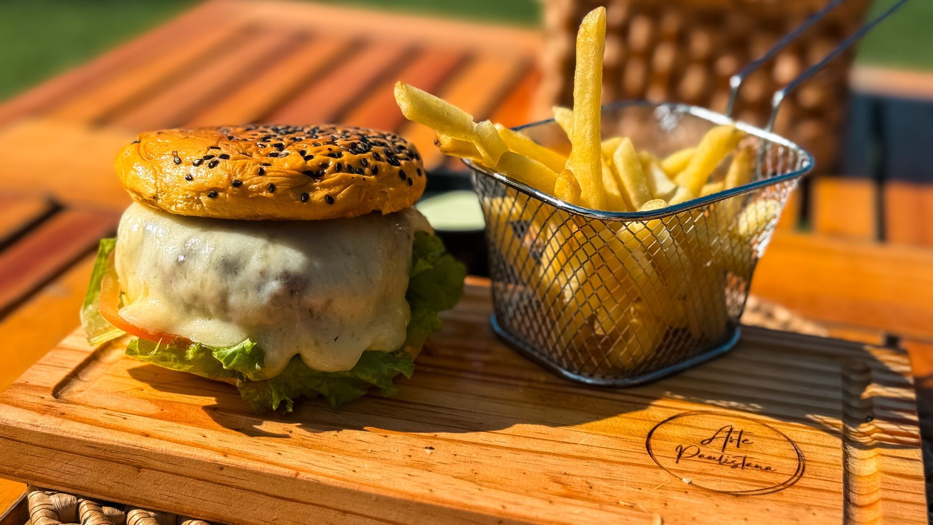 Uma mesa de jantar com tampo de vidro à beira-mar exibe pratos de comida, uma taça de vinho e uma bebida, com palmeiras ao fundo.