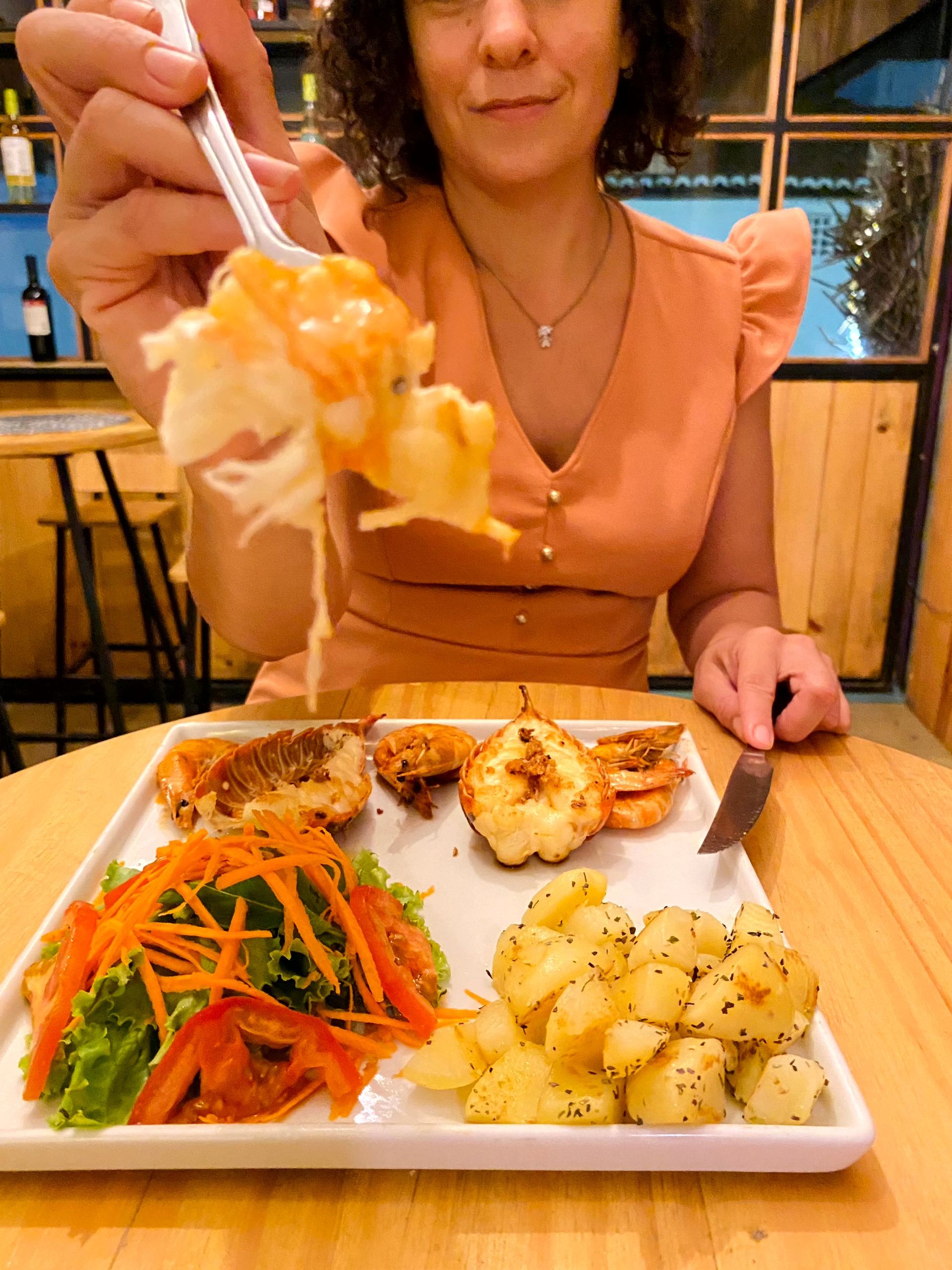 Uma mulher está sentada à mesa comendo um prato de comida.