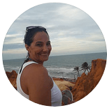 Uma mulher está no topo de um penhasco rochoso com vista para o oceano.