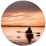 Uma pessoa está remando em um caiaque em um lago ao pôr do sol.