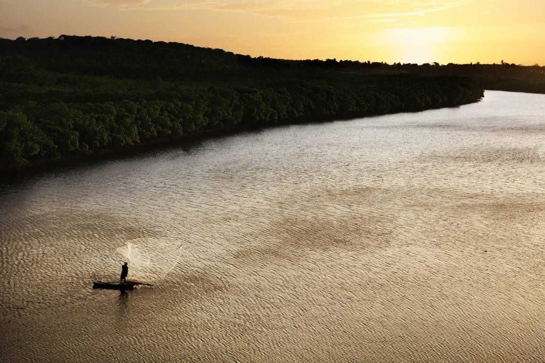 Um homem em um barco está pescando em um rio ao pôr do sol.