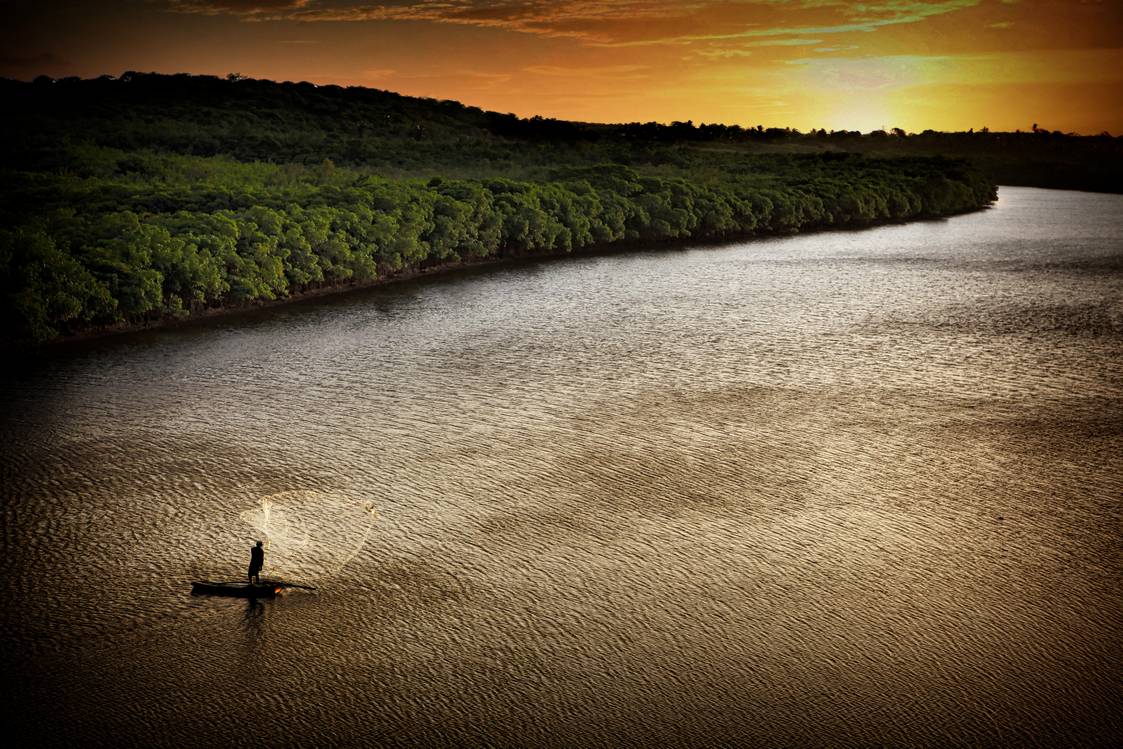 Uma pessoa está remando um barco em um rio ao pôr do sol.