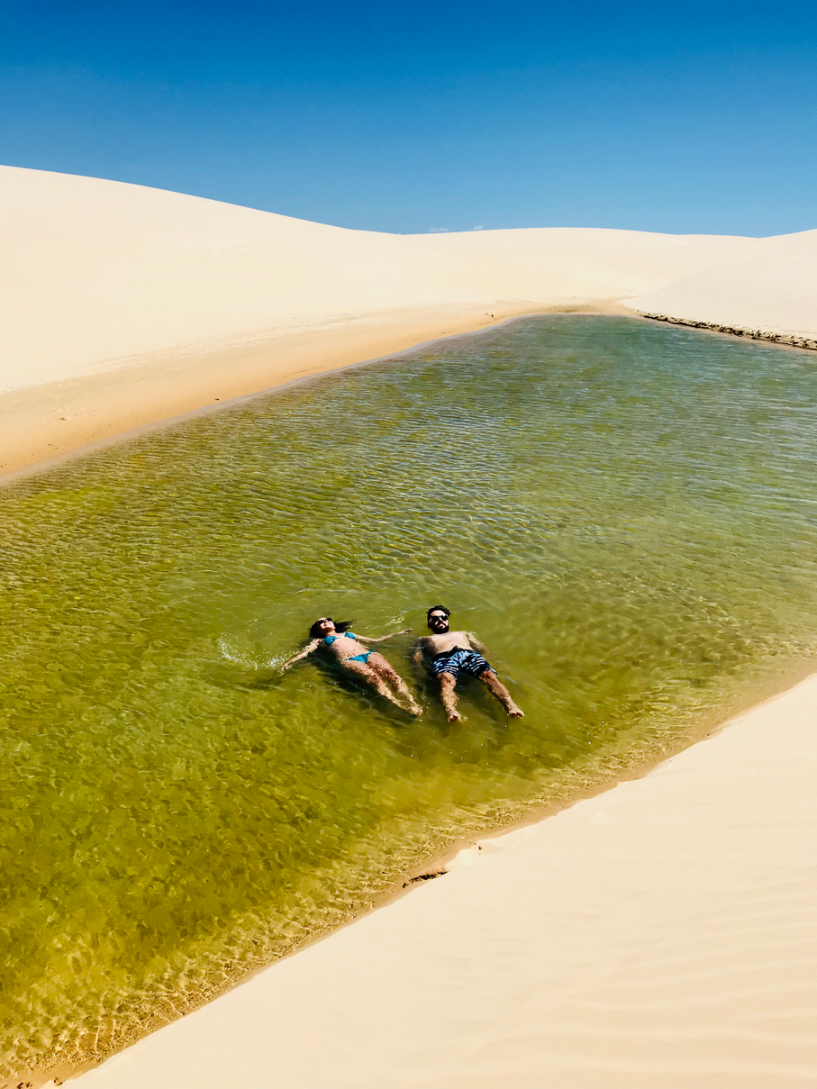 Duas pessoas estão nadando em um pequeno lago no meio de um deserto.