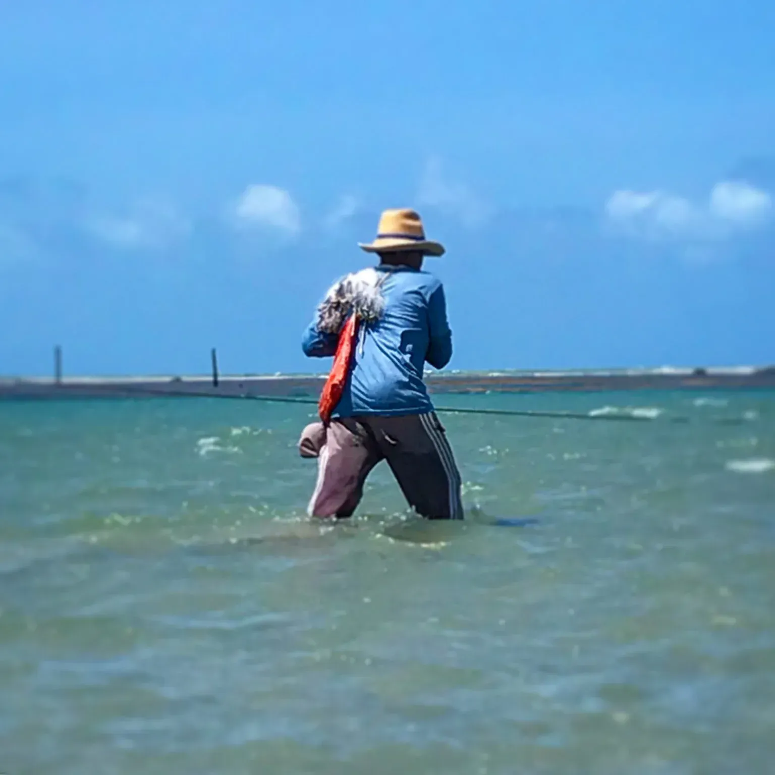 Um homem de chapéu está pescando no oceano