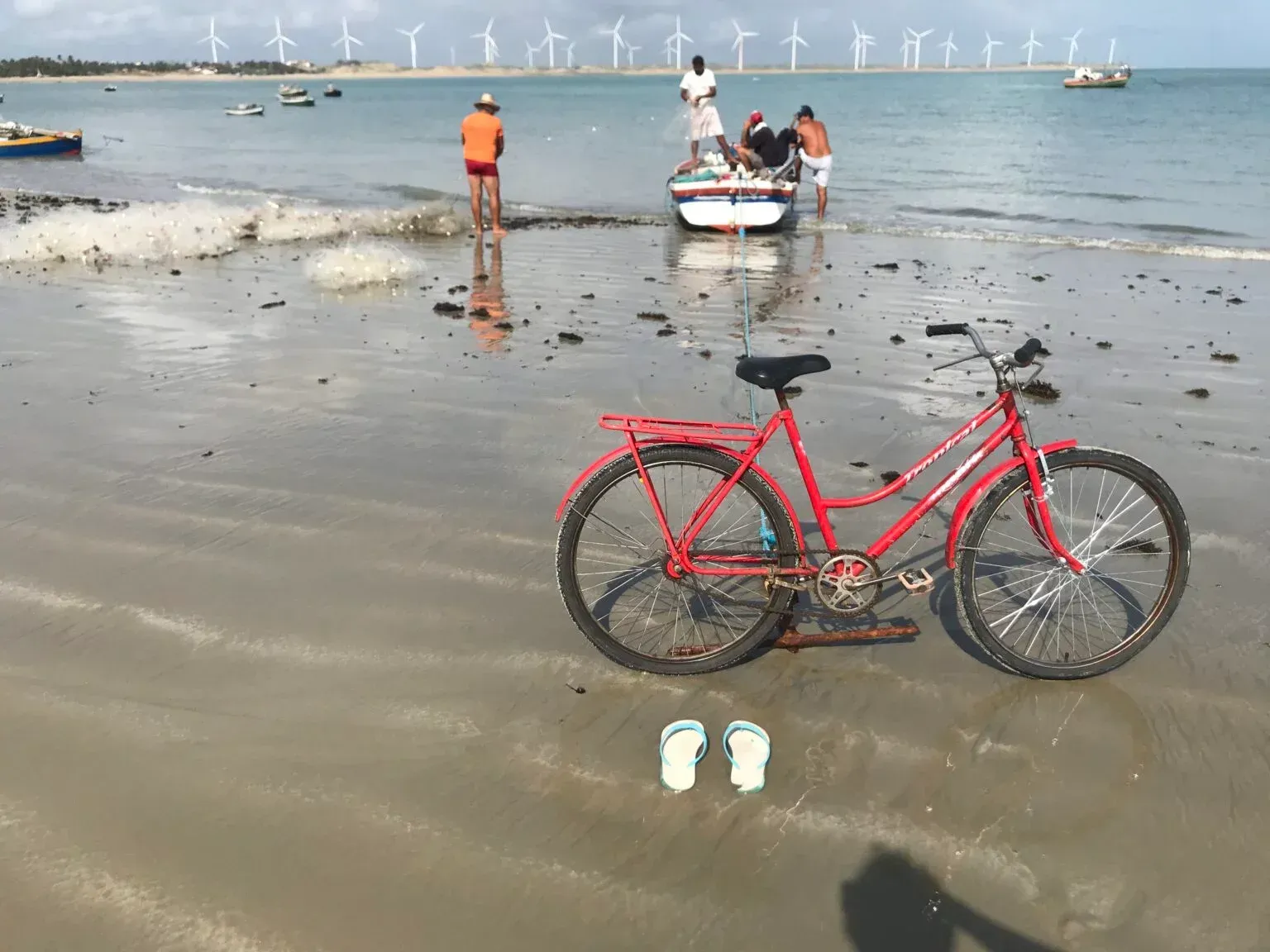 Uma bicicleta vermelha está estacionada na praia ao lado de um par de chinelos.