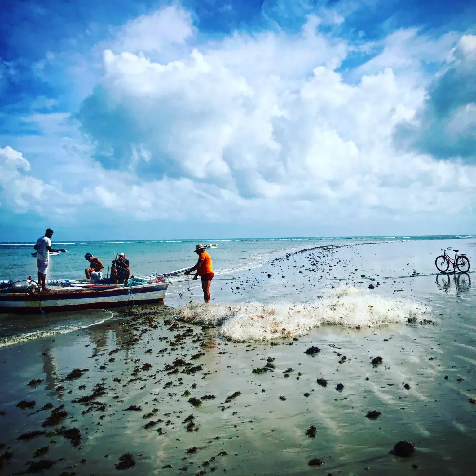 Um grupo de pessoas está pescando em uma praia perto de um barco