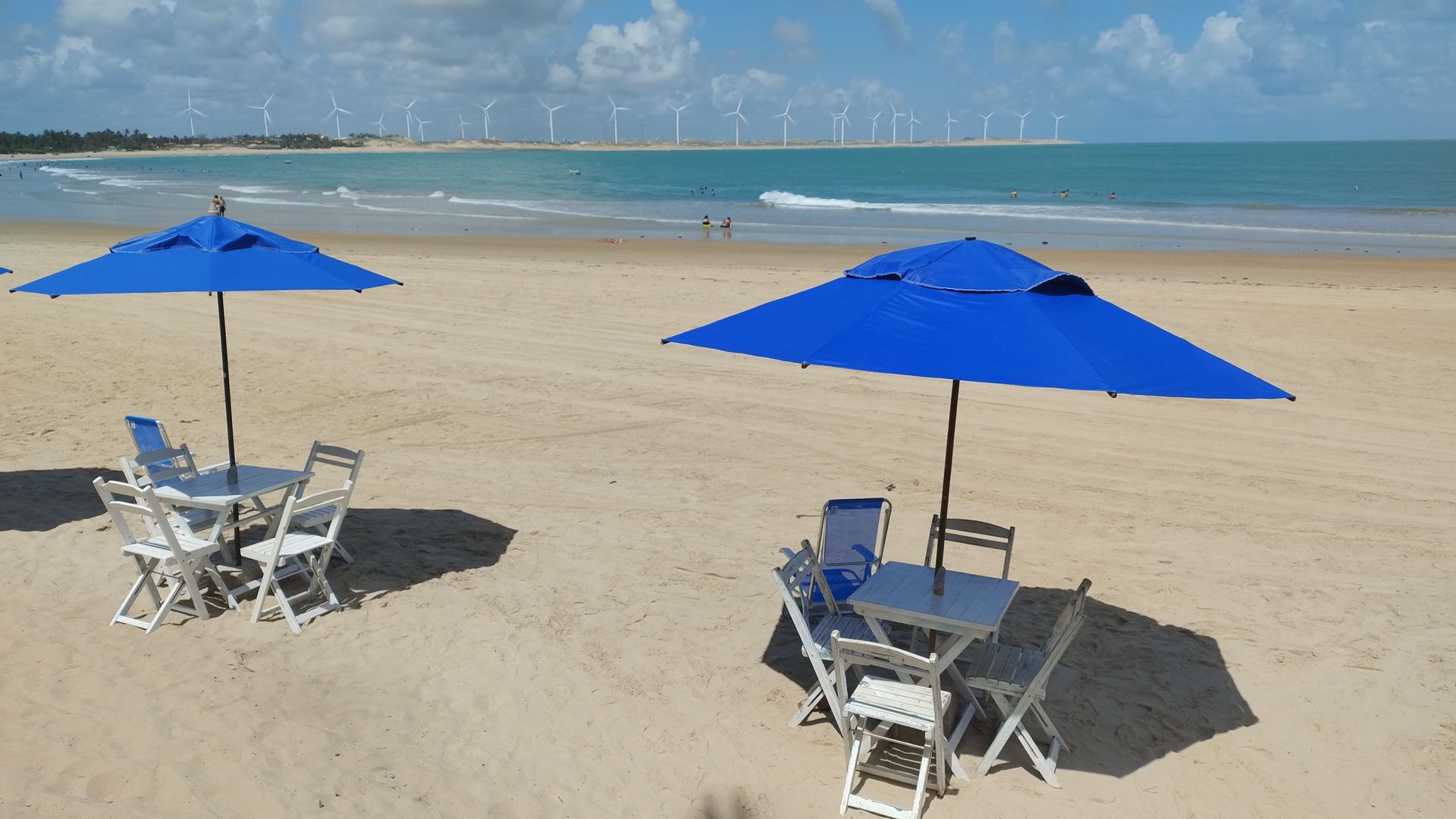 Uma praia com guarda-sóis azuis e mesas e cadeiras