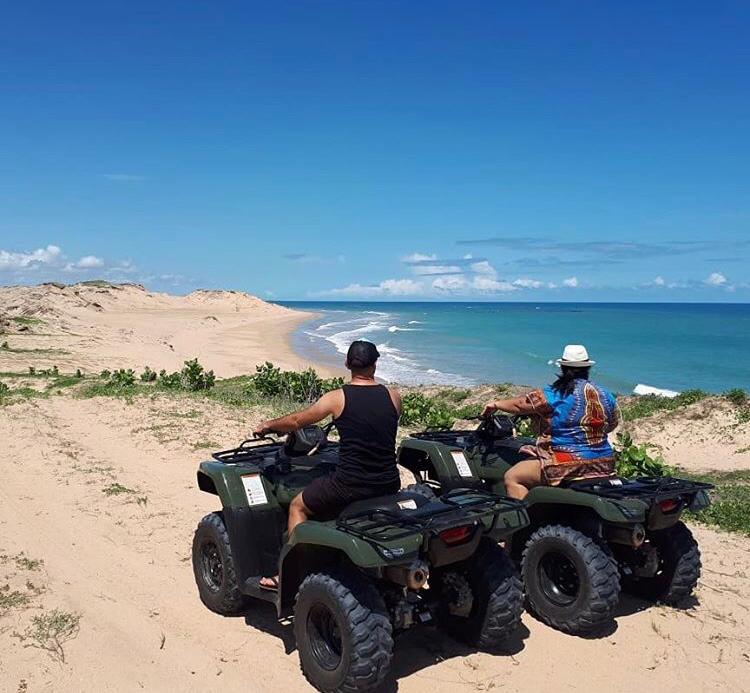 Duas pessoas estão andando de quadriciclo em uma praia perto do oceano