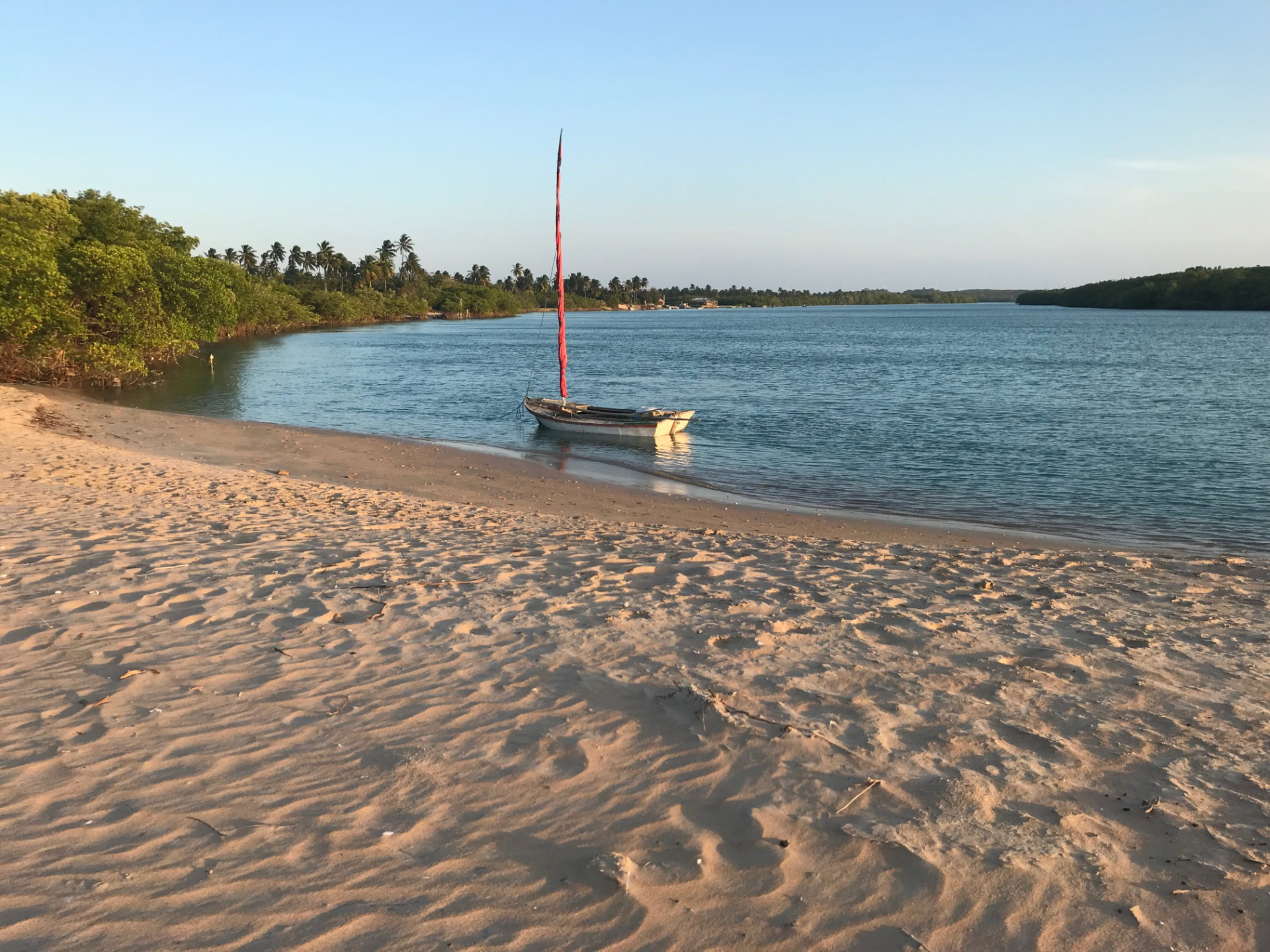 Um pequeno barco está parado em uma praia arenosa próximo a um corpo de água.