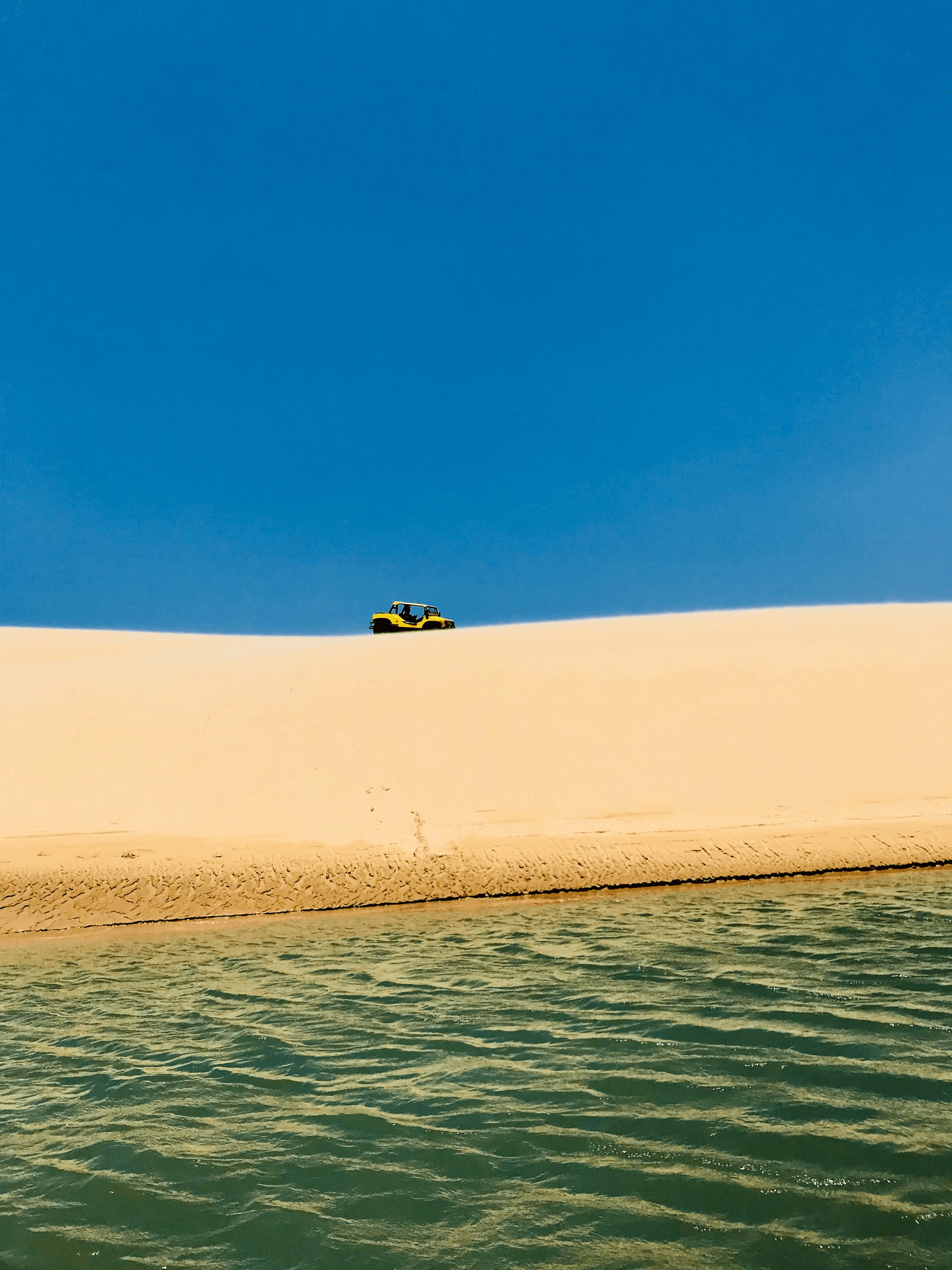 Um carro está passando no topo de uma duna de areia próximo a um corpo d'água.