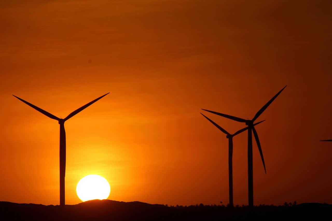 Duas turbinas eólicas são mostradas em silhueta contra um céu pôr do sol