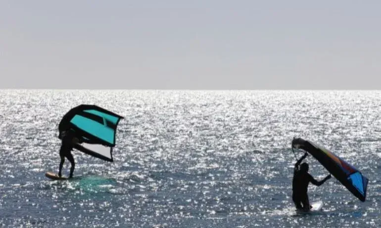 Duas pessoas estão empinando pipas no oceano.