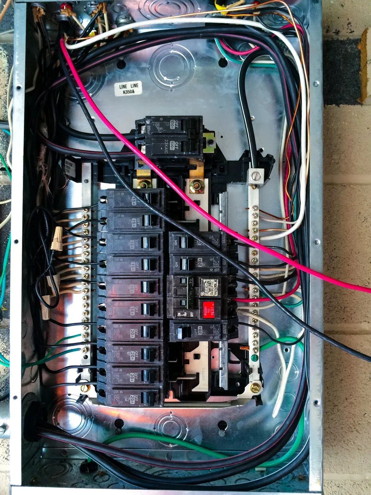 Electrical panel with various colored wires and circuit breakers inside a metal box.