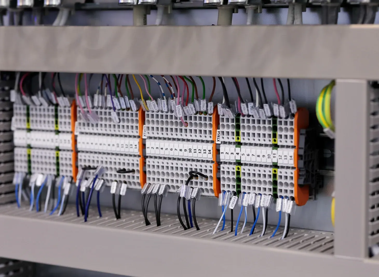 Wires connected to terminal blocks inside an electrical cabinet. Various colored wires and orange dividers.