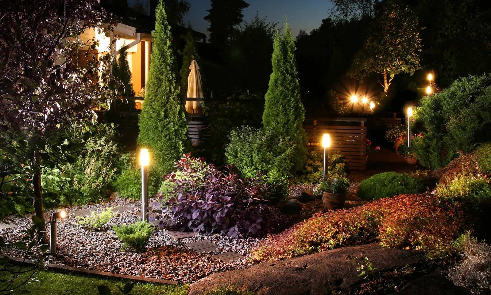 Lit garden bed at night; decorative lights illuminate trees and bushes.