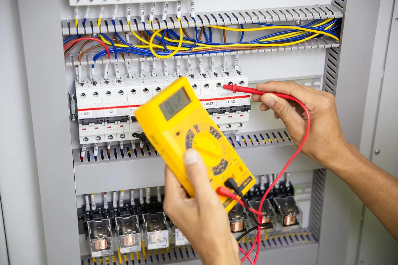 Person using a yellow multimeter to check the electrical wiring inside a control panel.