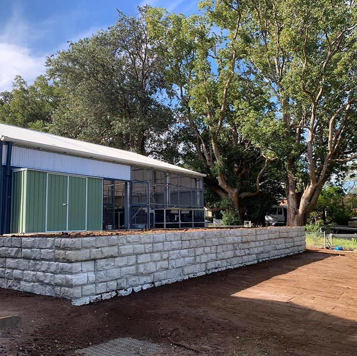 A Brick Wall Is In Front Of A Building With Trees In The Background — Bennett's Environmental In Ulladulla, NSW