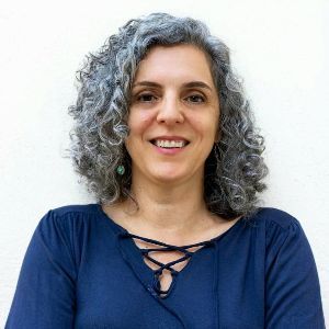 Uma mulher de cabelos grisalhos e camisa azul está sorrindo.