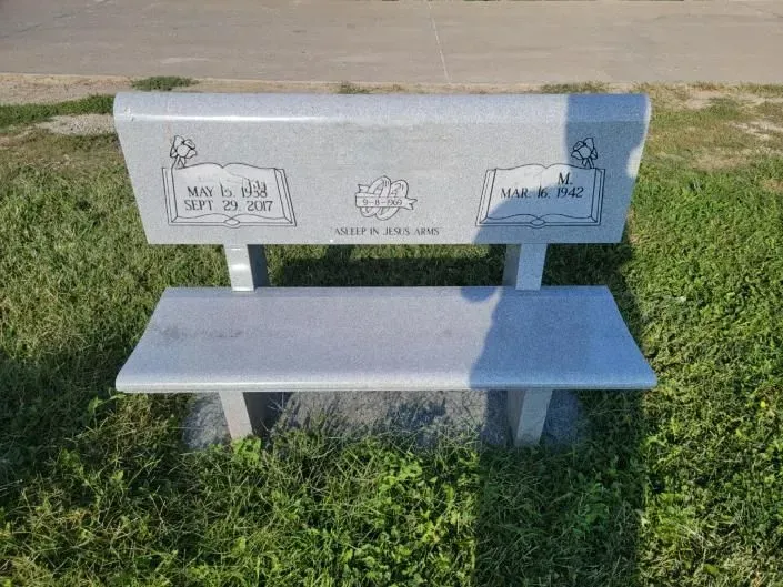 A stone bench is sitting in the grass in a park.