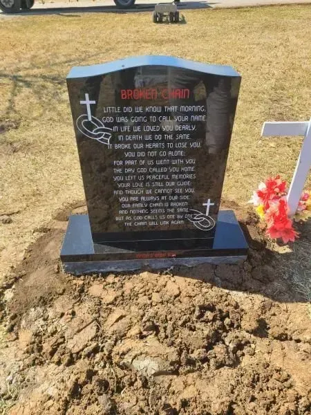 A gravestone in a graveyard with flowers and a cross
