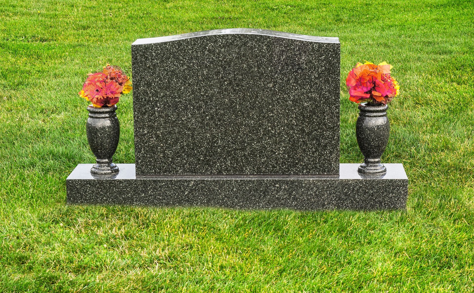 A vase is sitting on a granite ledge next to a grave.